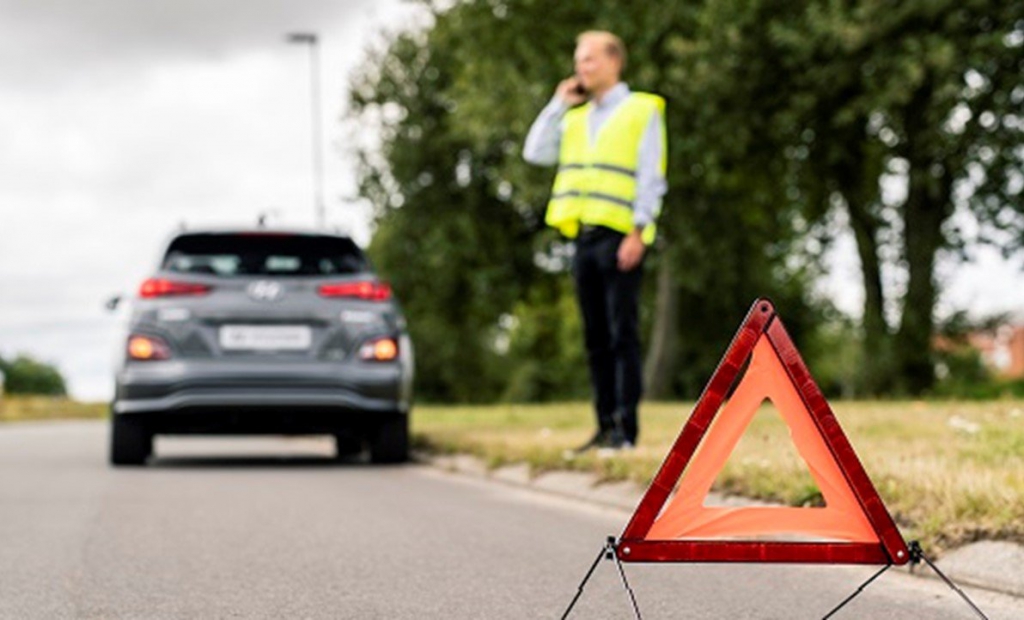 Man med reflexväst och varningstriangel samt en grå Hyundai