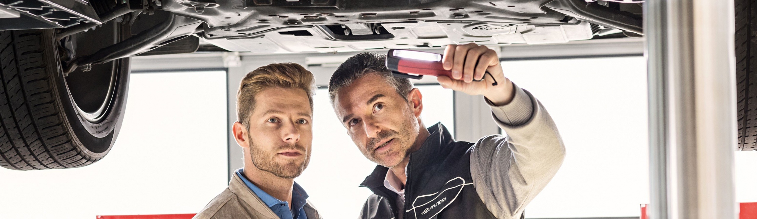 Två personer kollar unden bilen med ficklampa RA Motor