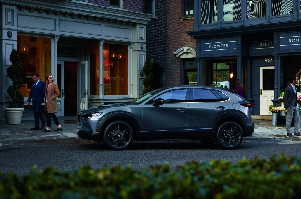 Grå Mazda CX-30 parkerad i stan med folk runtom