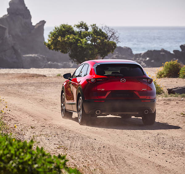 Röd Mazda CX-30 kör på grusväg vid havet