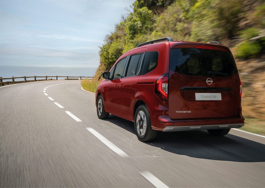 Röd Nissan Townstar Combi kör på landsväg längs med vattnet