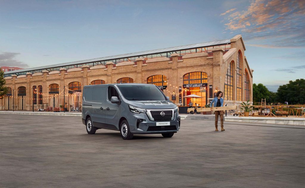 Grå Nissan Primastar parkerad utanför en restaurang och en man som bär på plankor brevid