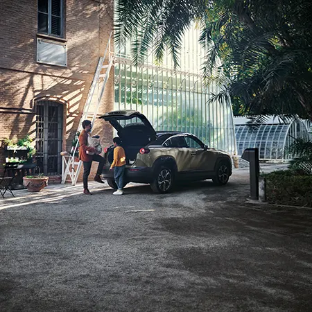 Mazda MX-30 R-EV Makoto utanför ett växthus med en far och dotter bredvid