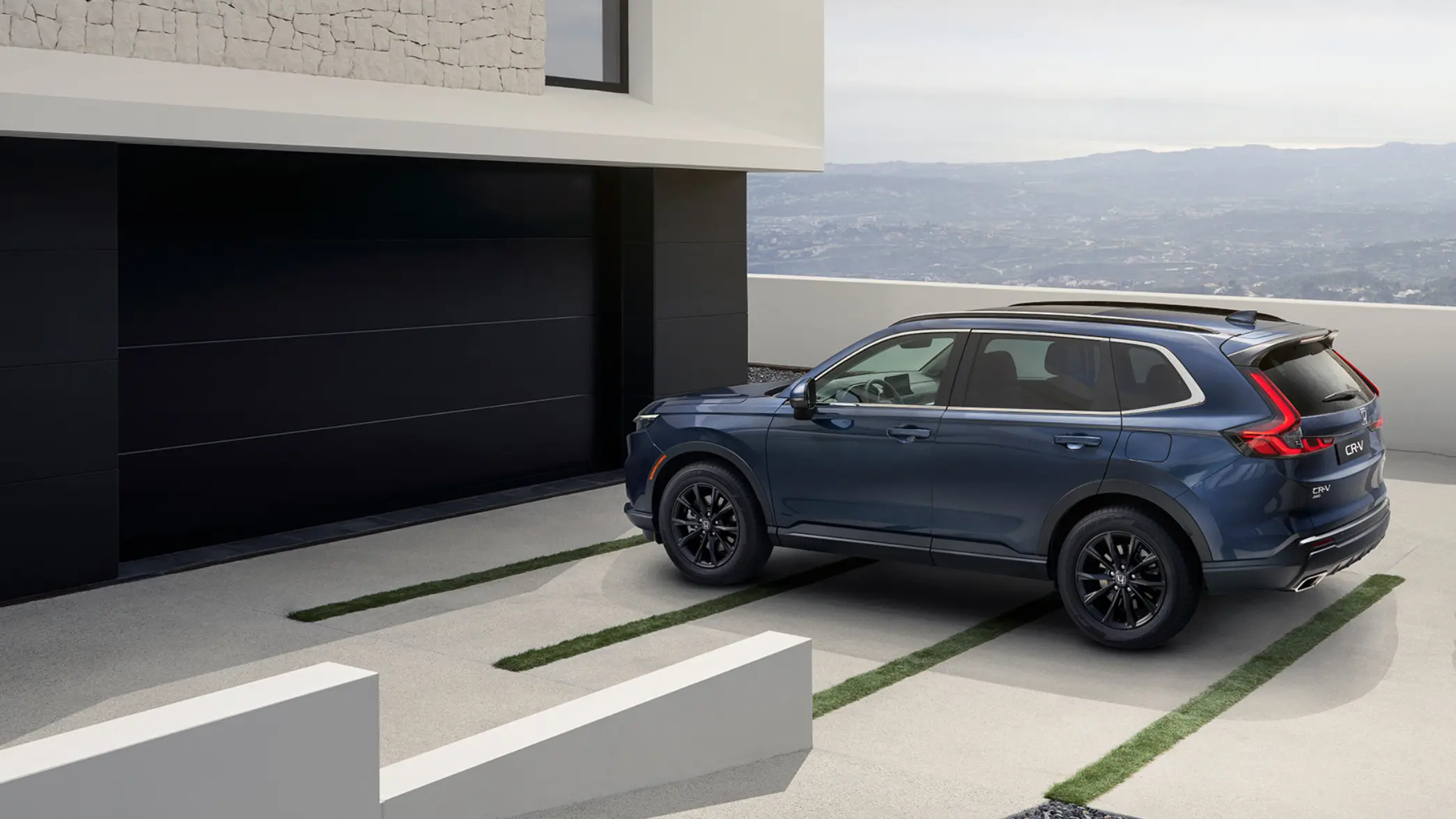 Blå Honda CR-V e:HEV fullhybrid parkerad på garageuppfart med havet i bakgrunden