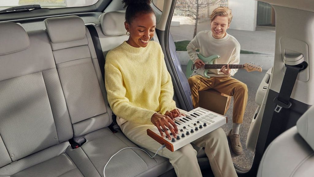 KONA Electric 2023 - tjej spelar keyboard i baksätet inkopplat till V2L
