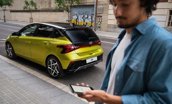 Kille som håller i en telfonmmed Bluelink framför en Hyundai i20 i färgen Lucid Lime