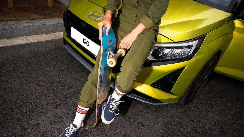 Kille med skateboard lutar sig mot en Hyundai i20 i färgen Lucid Lime