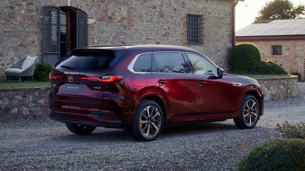 Mazda CX-80 i färgen artisan red parkerad utanför en vacker gårdsbyggnad