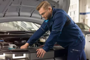 Bild tillhörande knappen "Boka bilservice" - ett mekaniker som inspekterar under huven på en Hyundai